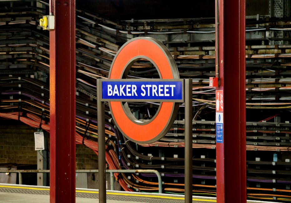 A close-up view of a London Underground station sign displaying 'Baker Street' on a blue background within a circular red frame, mounted on black metal supports. Behind the sign, there is a wall with neatly organized stacks of wooden and metal rail track components, with some orange and purple cables visible. The scene is illuminated with natural light, highlighting the clean, well-maintained surfaces and materials, which include metal and wood. This image exemplifies surface cleaning and maintenance in an urban transit environment, relevant to residential and commercial cleaning practices discussed on the page, and reflects the professional cleaning services offered by Marylebone Cleaners.