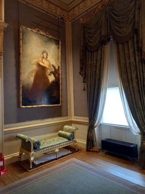 A section of a luxurious room featuring a large window with ornate, heavy drapes in dark green and gold, partially drawn to reveal bright natural light. The wooden floor is polished, and a light-colored area rug covers part of the floor. Against the wall, there is an elegant upholstered bench with a carved wood frame, padded armrests, and matching pillows. Above the bench, a large framed oil painting of a woman in a historical dress hangs on the wall, which is decorated with intricate crown molding and gold trim. The room exudes opulence and classical interior design, consistent with the sophisticated setting of the Wallace Collection Apartment Care in Marylebone. Marylebone Cleaners provides professional domestic cleaning to maintain such refined spaces, ensuring surfaces remain spotless and well-maintained.